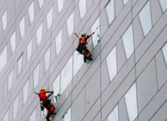 Dos operarios descolgados trabajando sobre la fachada acristalada de una torre