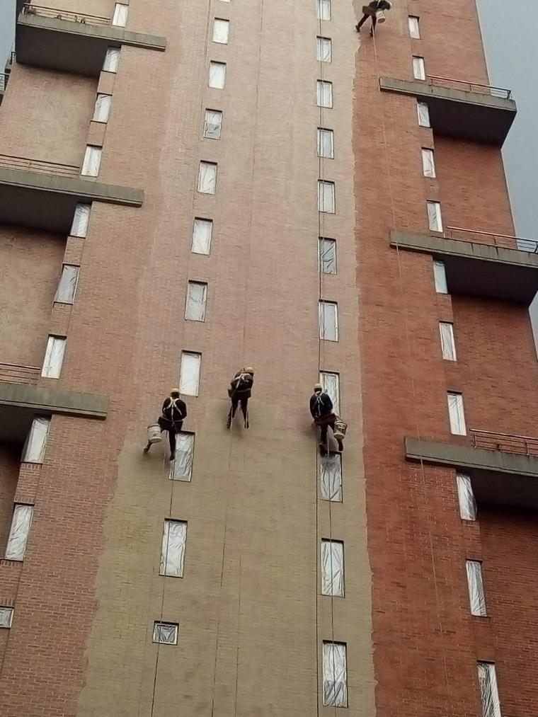 Cuatro operarios descolgados pintando la fachada de ladrillo de una torre residencial