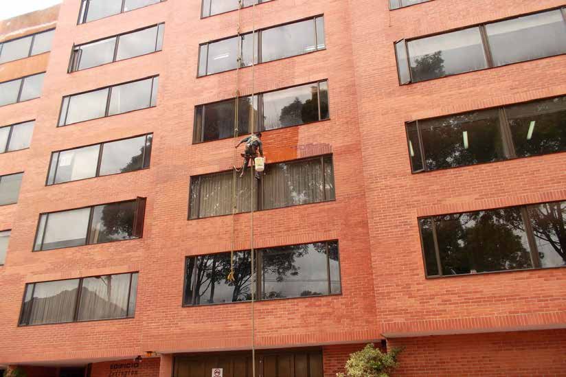 Operario descolgado pintando la fachada de ladrillo de un edificio residencial
